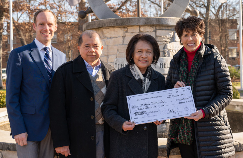 Four people standing outside holding an oversized check