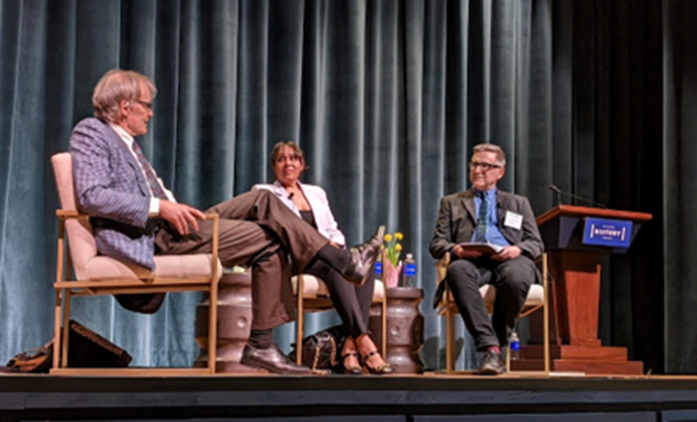 Three seated panelists on stage