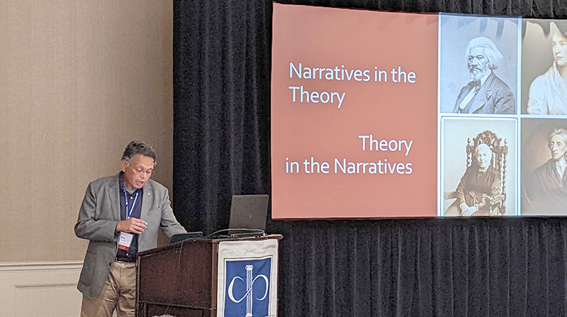 presenter at podium with slide on narratives in the theory on screen