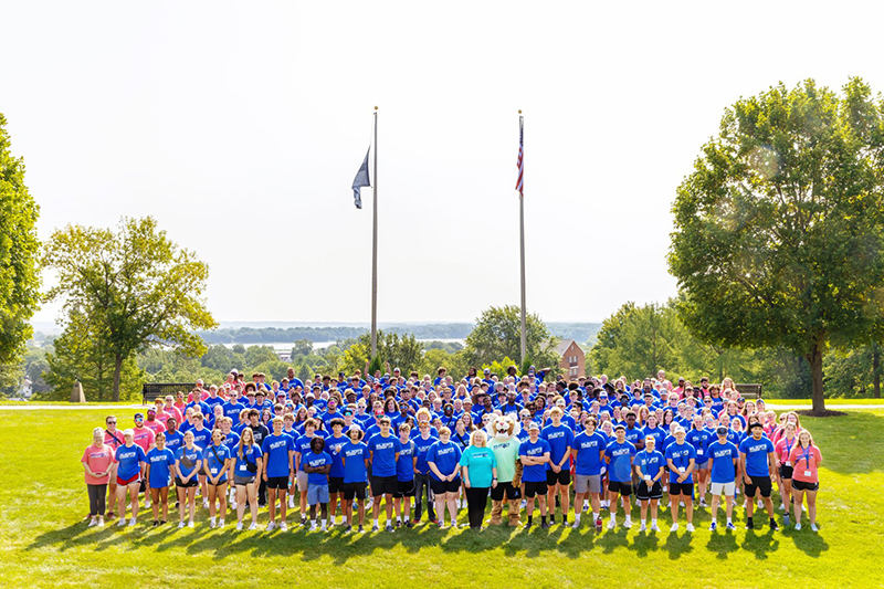 large group of students and faculty standing outside on a hill