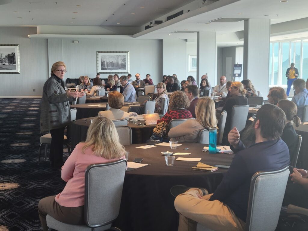 Kathleen Rinehart presents while standing to participants seated at roundtables