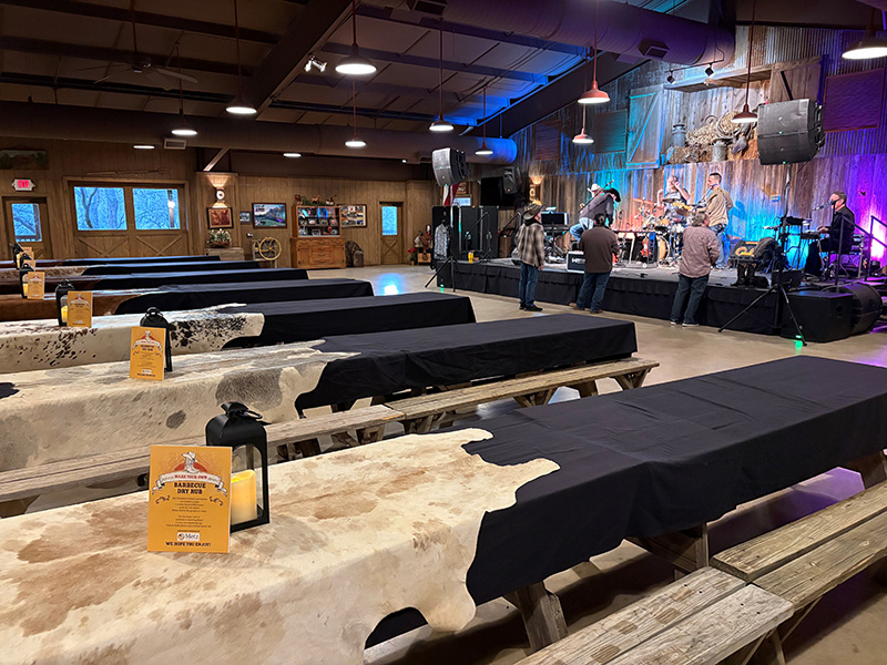 Cowhide covered tables inside ranch hall with live band warming up on stage