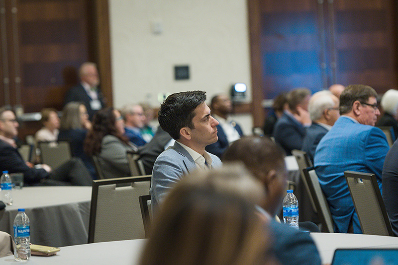 Participants seated at roundtables listen to speakers
