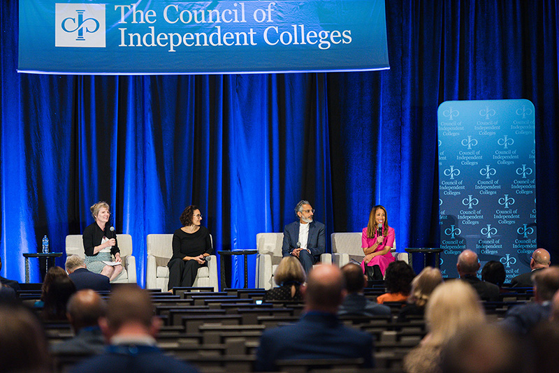 Four panelists seated on stage answer questions from seated participants