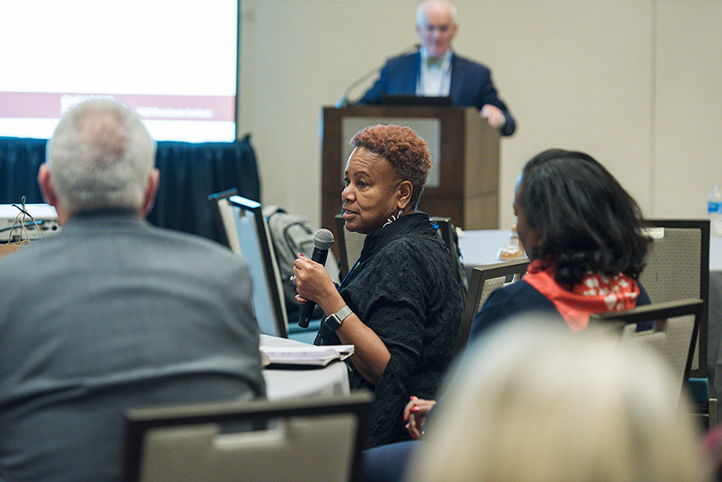 Seated participant with microphone speaks to colleagues during session