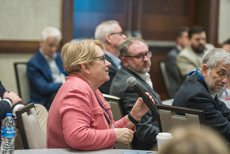 Participant seated at roundtable holds mic to ask question