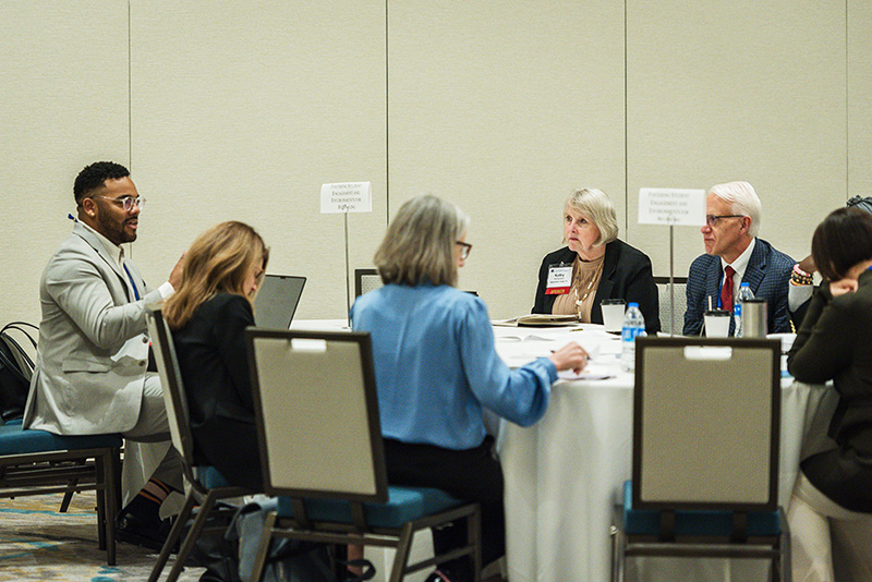 participants seated at roundtable discussion table with placards denoting the table's topic