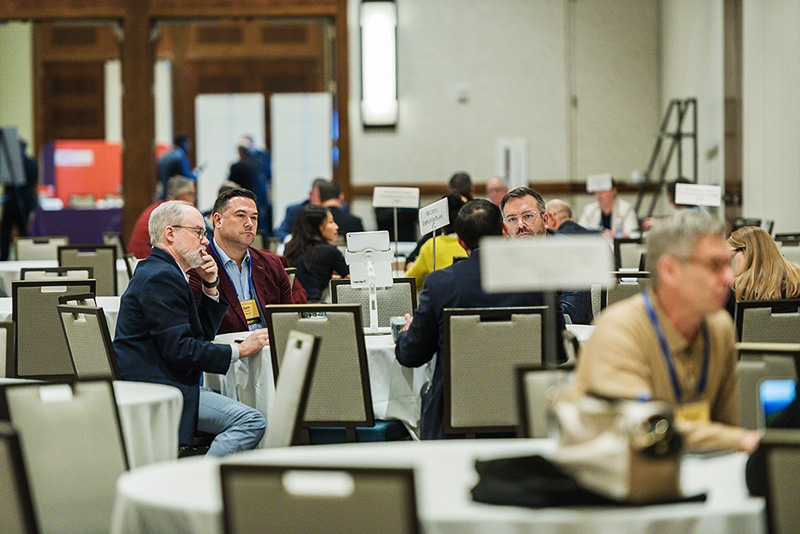 participants seated at roundtable discussion tables with placards denoting the table's topic