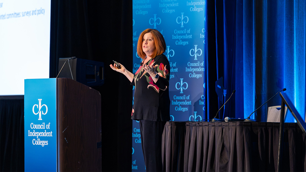 Plenary speaker stands on stage holding a slide advancer