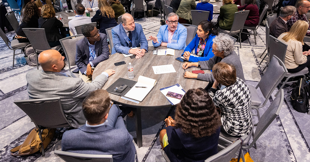 Nine participants share ideas while seated at a roundtable