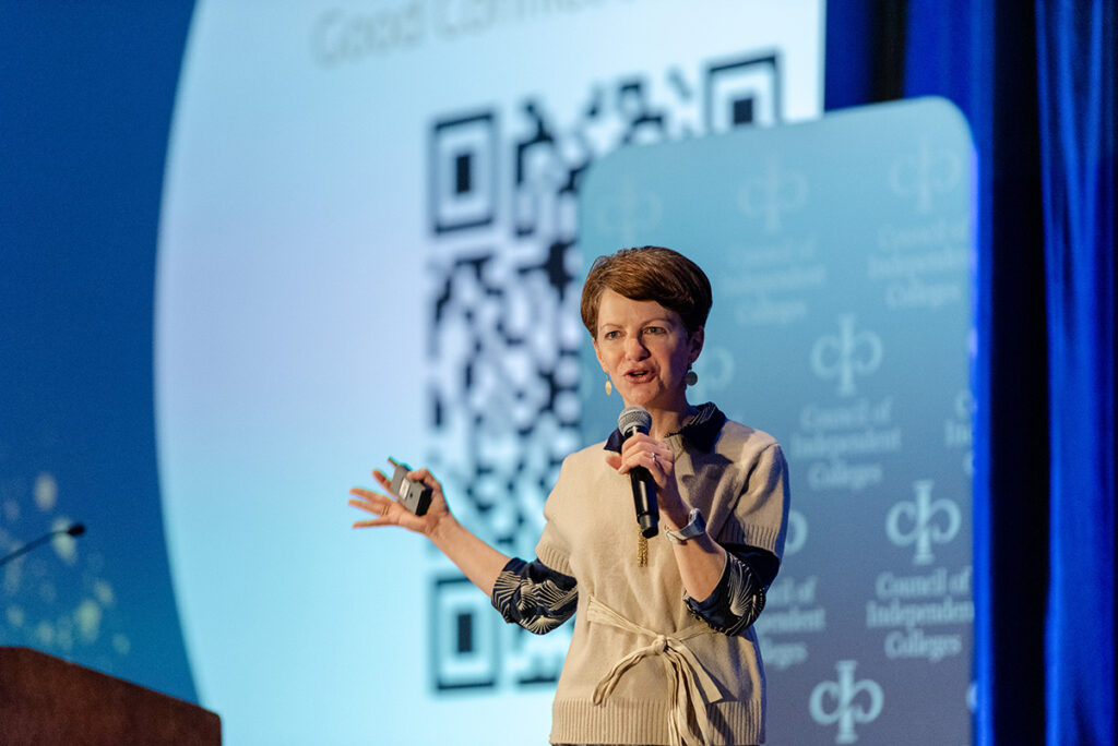 Plenary speaker stands on stage holding microphone and slide advancer