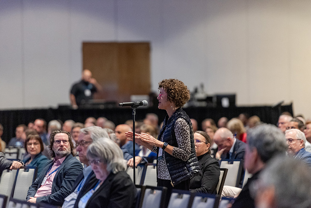 College president stands at microphone to ask question during plenary session