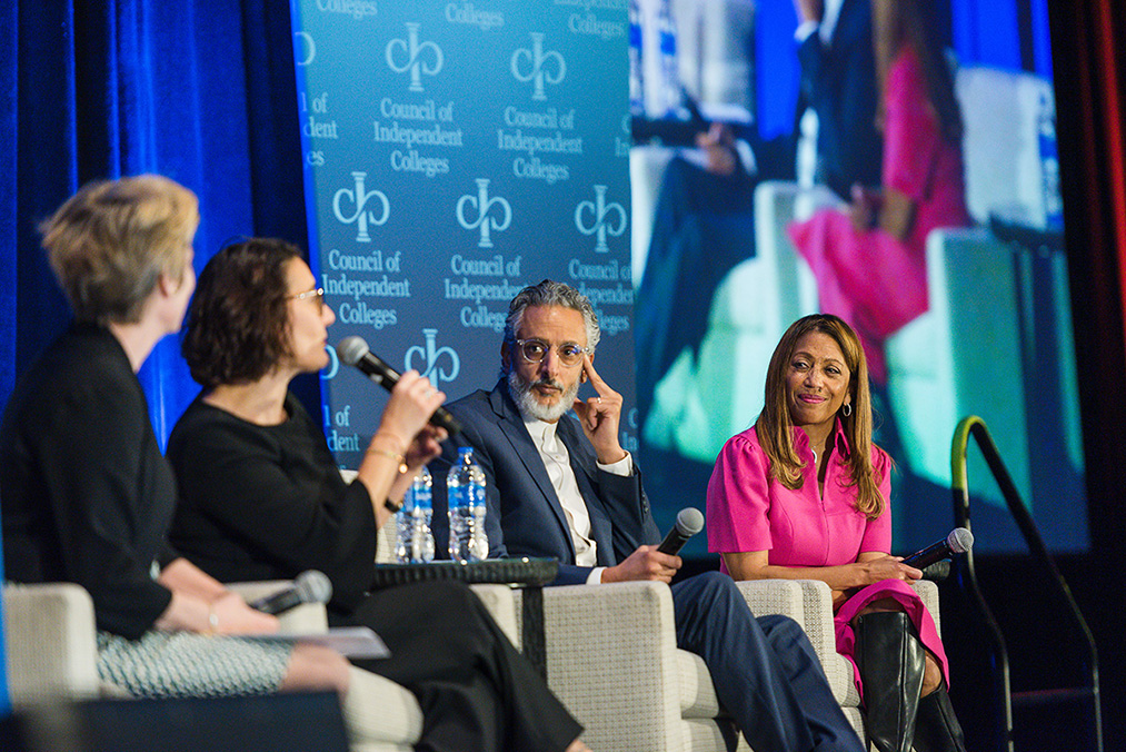 Four seated panelists on stage speaking into handheld microphones