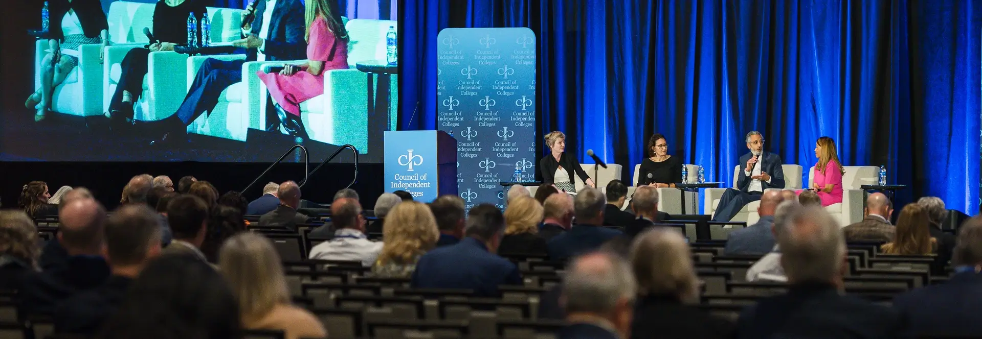 Four seated panelists speaking on stage in front of seated Institute participants